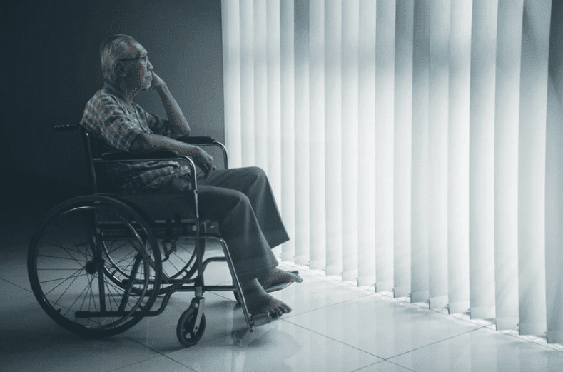 Old man sitting on wheelchair while looking at window