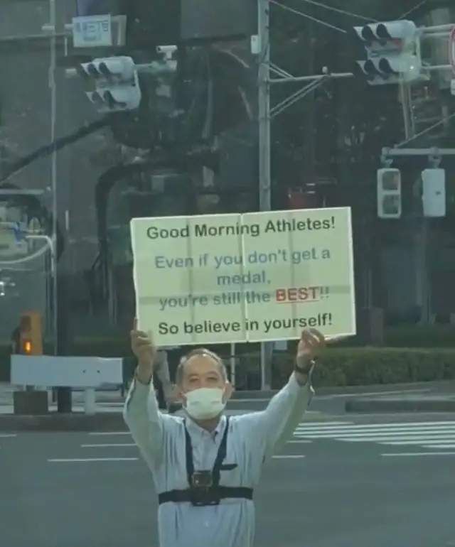 Japanese man holds up sign to encourage athletes outside the olympic village every day | weirdkaya