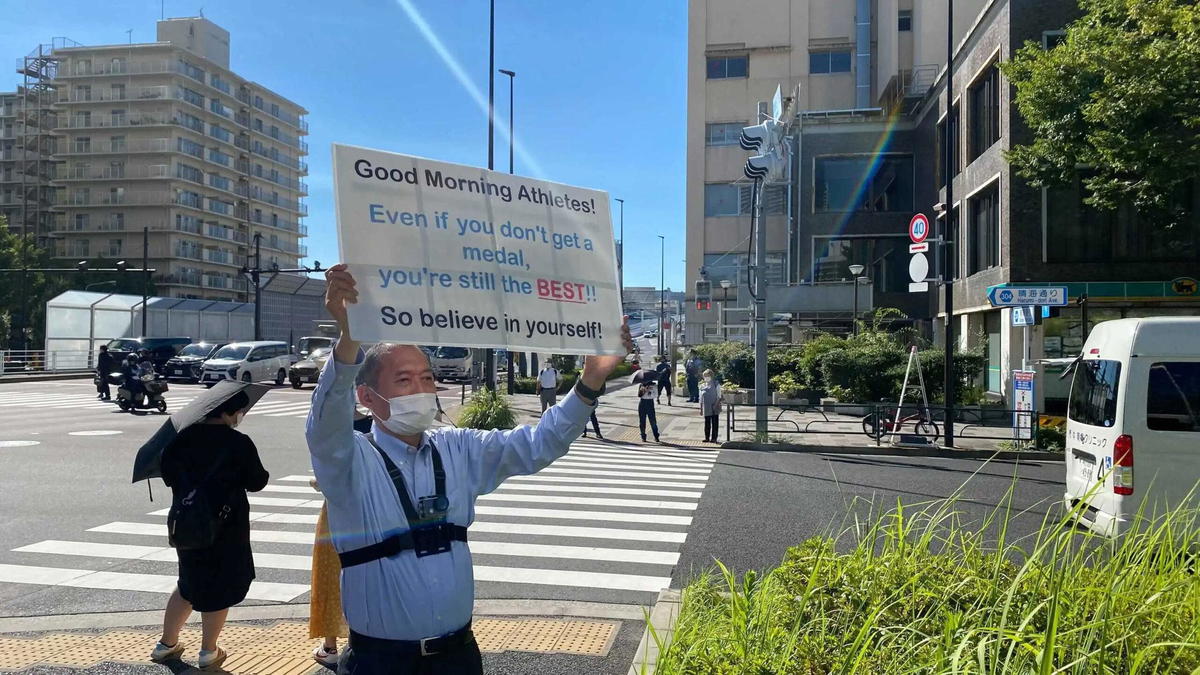 Japanese man holds up sign to encourage athletes outside the olympic village every day | weirdkaya