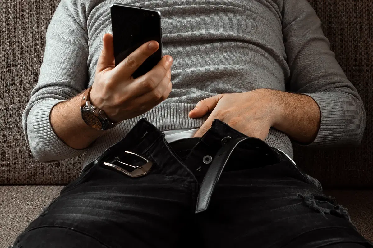 Man putting his hand inside his pant while holding a phone.