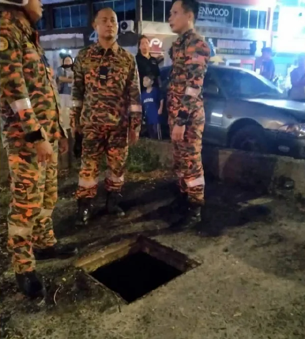 Firefighters standing near manhole which boy fell into