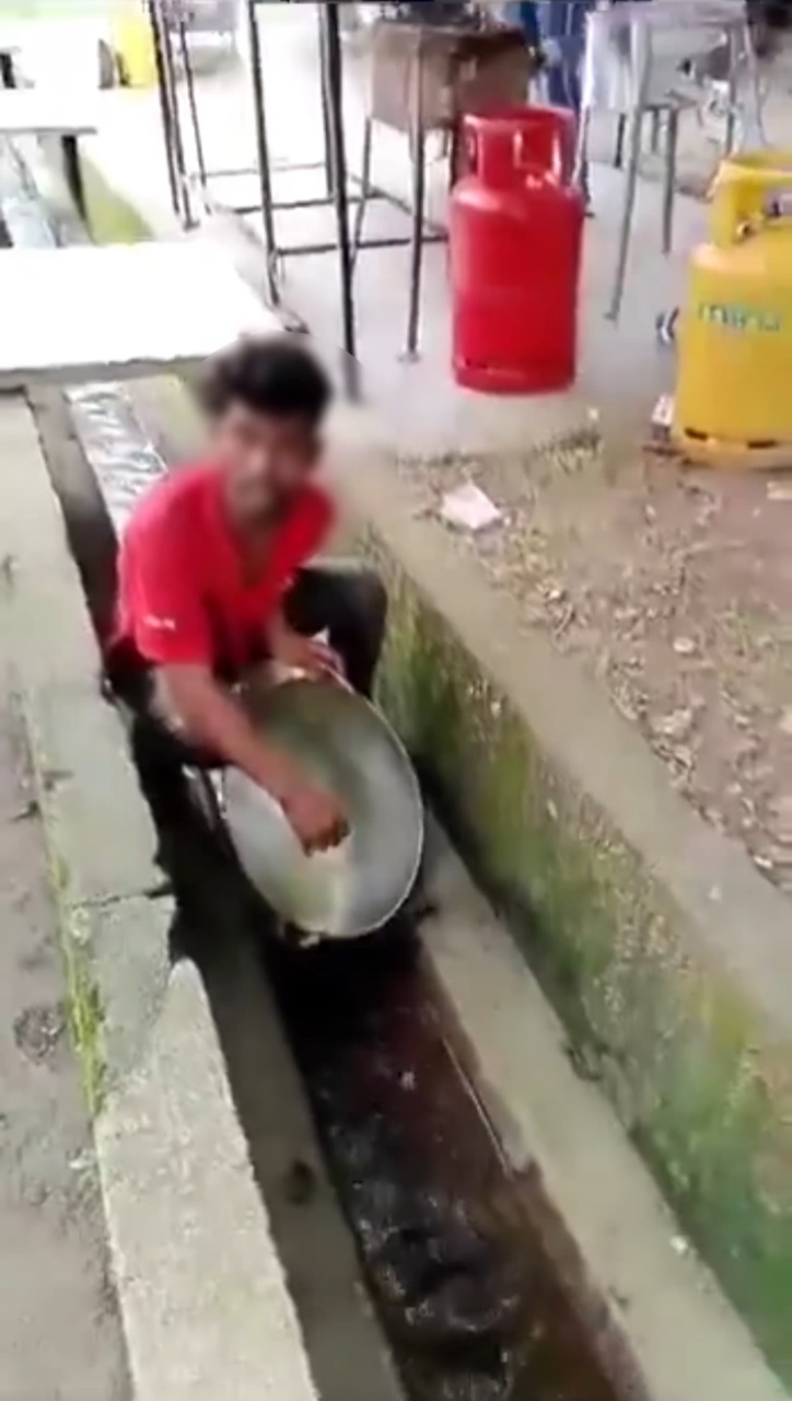 Foreign worker washing wok inside the drain