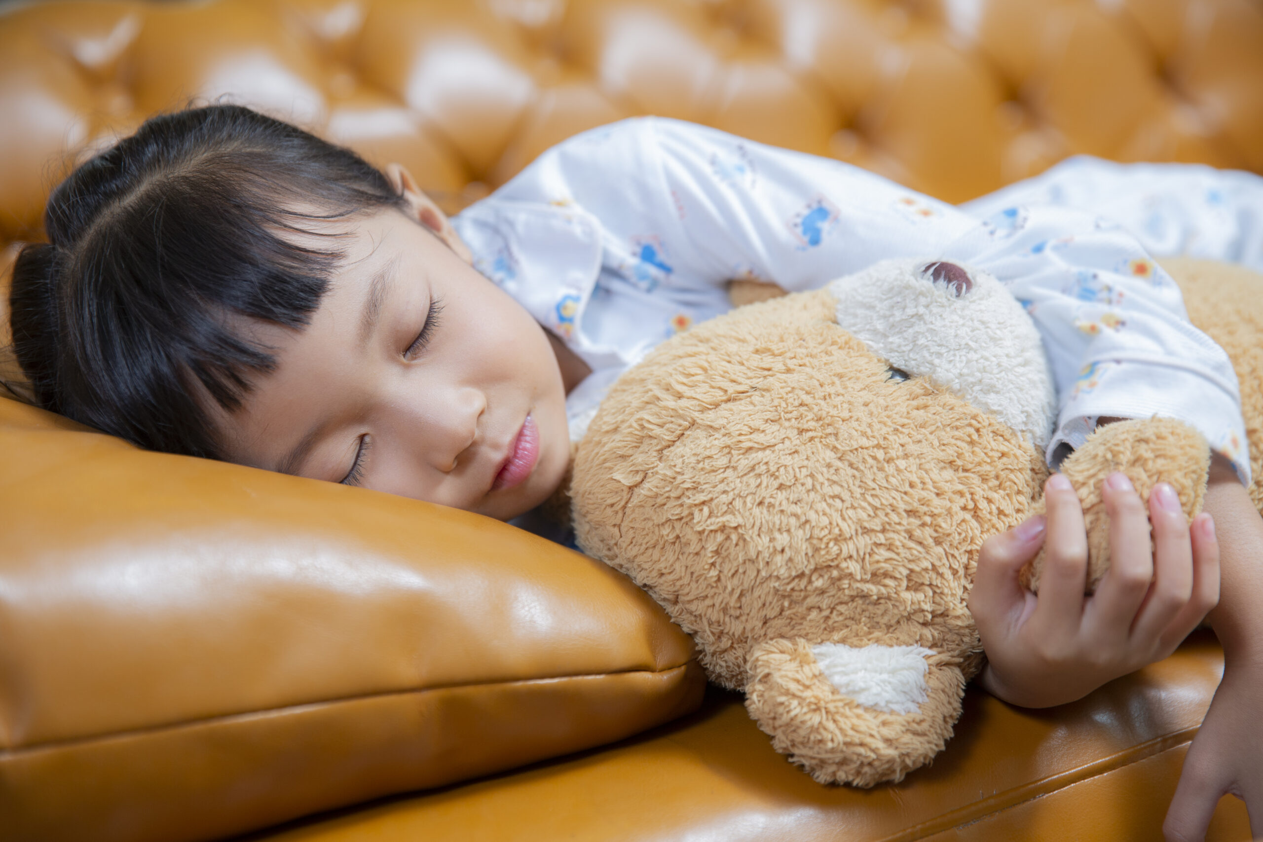 Young girl sleeping with teddy bear on sofa