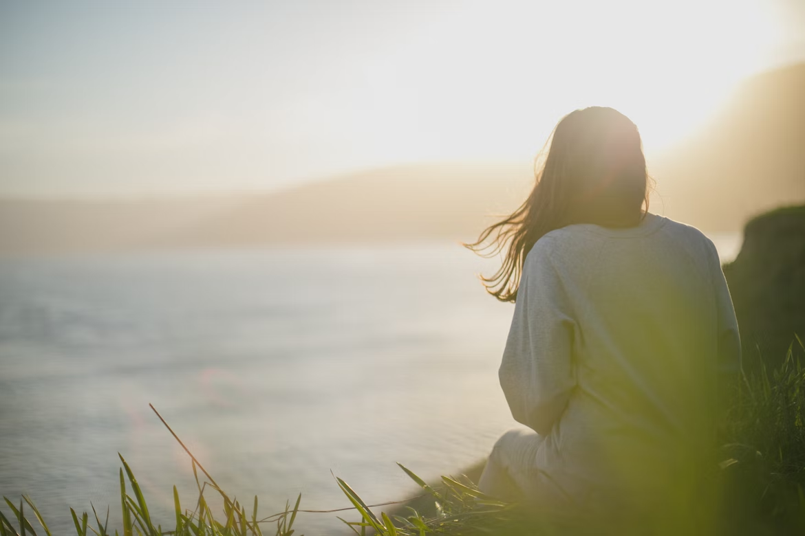 Woman reflecting while sitting alone beside a lake