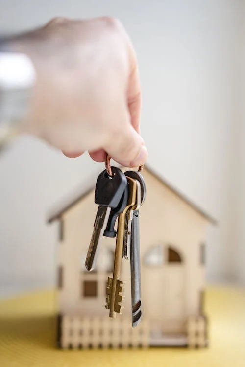 A person holding a set of keys with a house in the background