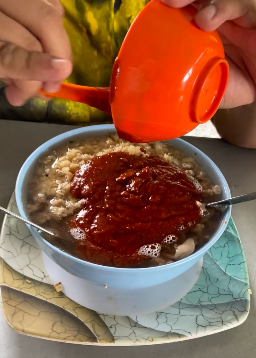 Man pours full bowl of sambal into his bihun soup at kedai bihun sup zaman - july 2024