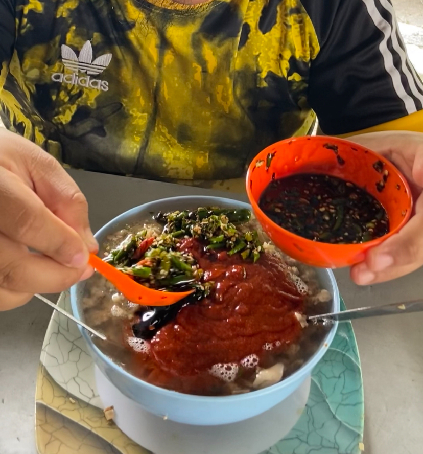 Man pours full bowl of sambal into his bihun soup at kedai bihun sup zaman - july 2024