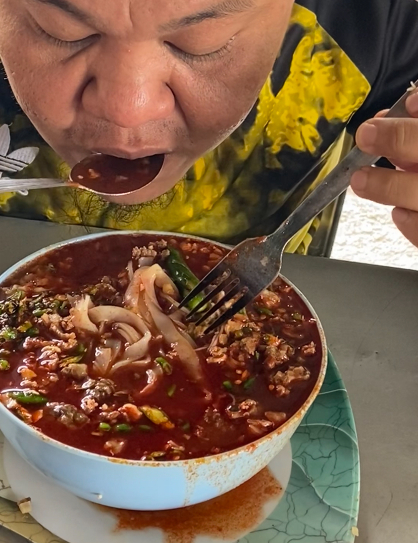 Man pours full bowl of sambal into his bihun soup at kedai bihun sup zaman - july 2024