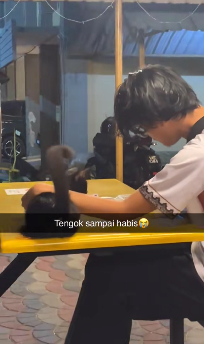 M'sian student having a meal accompanied by black cat