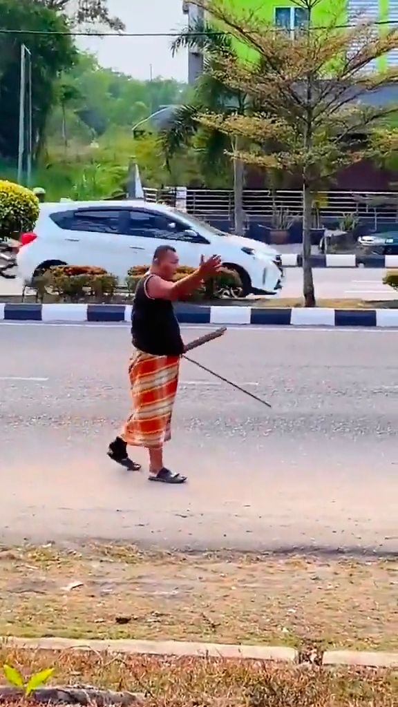 M'sian uncle dressed in sarong waves wooden stick at mat rempits on 1st day of raya
