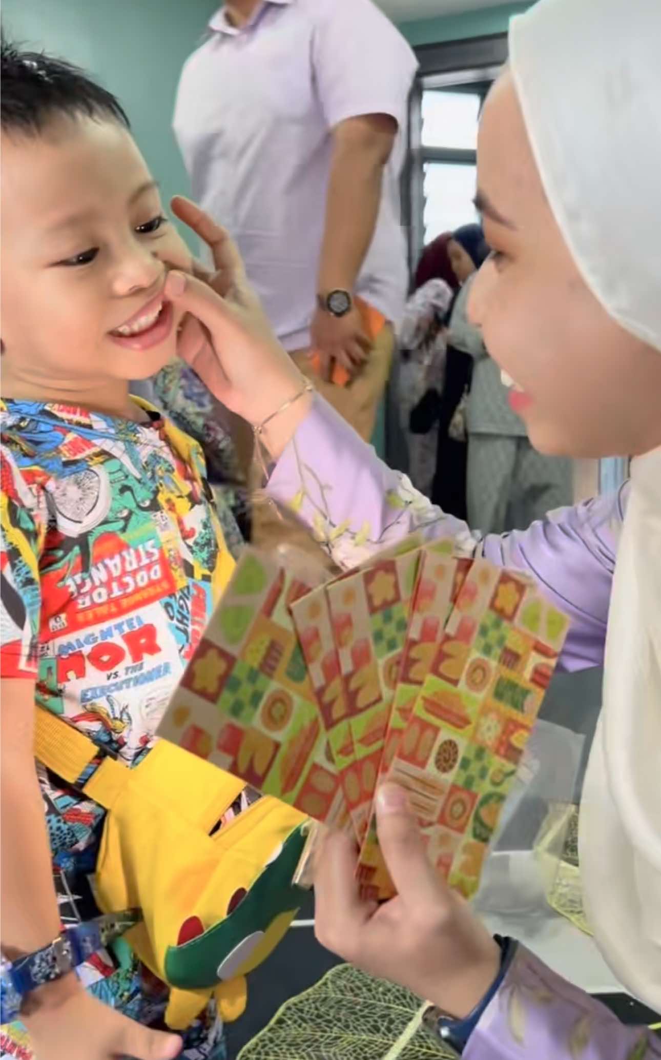 Boy shows his teeth before taking his duit raya packet