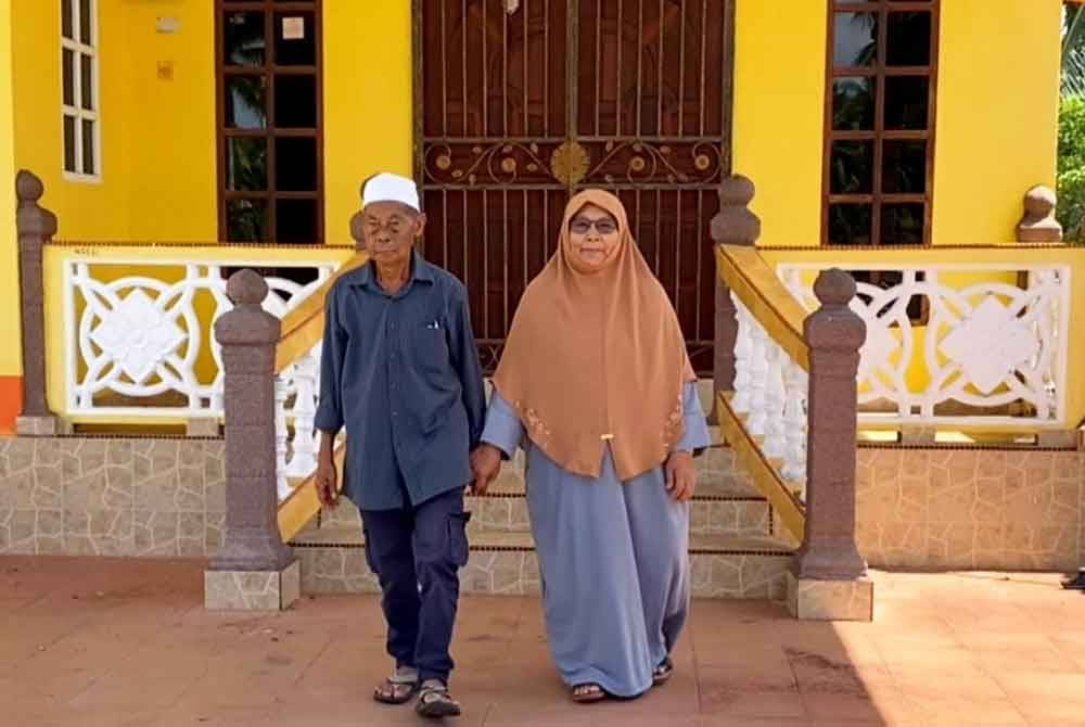 Msian elderly couple standing infront of their house