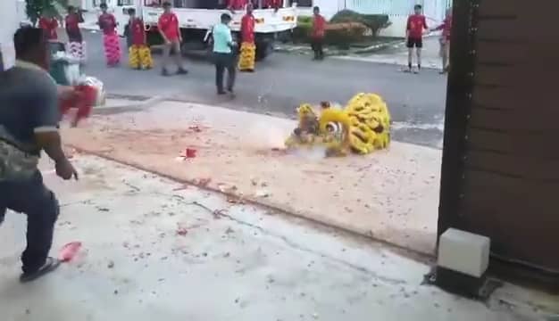 Msian man throwing firecracker towards teh lion dancers