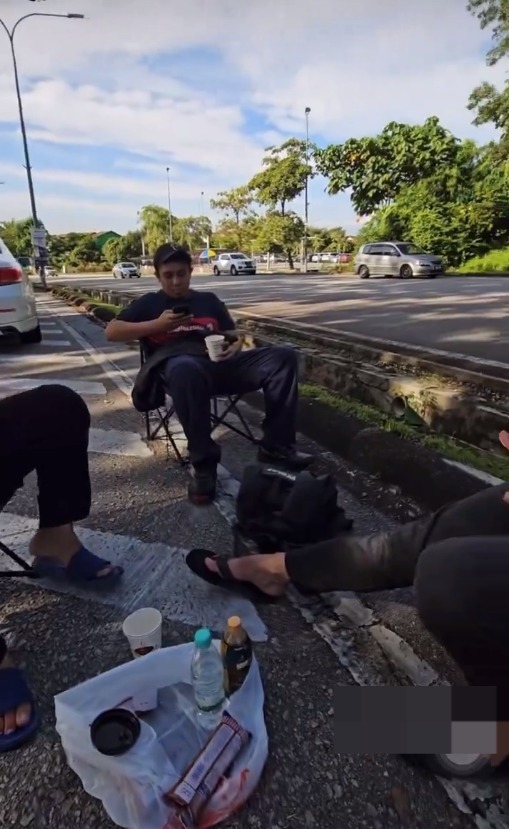 Msian men casually sitting by the roadside using their phone