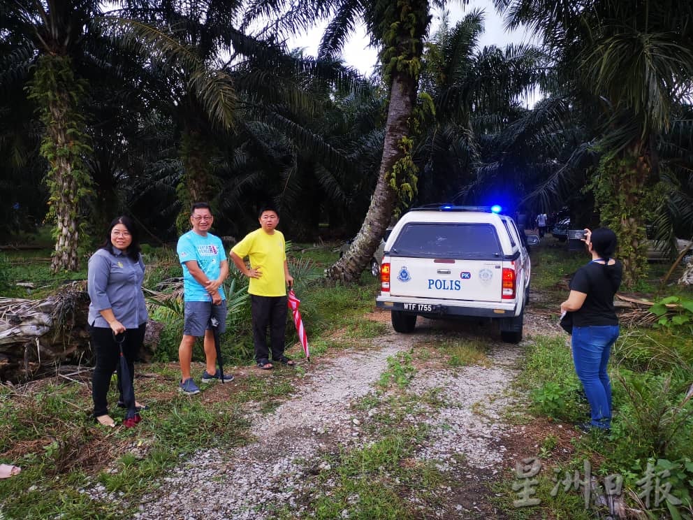 Bystanders and police car at palm oil plantation where the murder took place