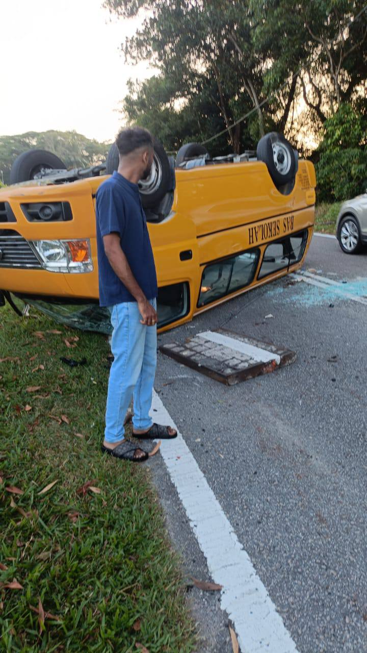 Passerby looks at overturned bus in Johor