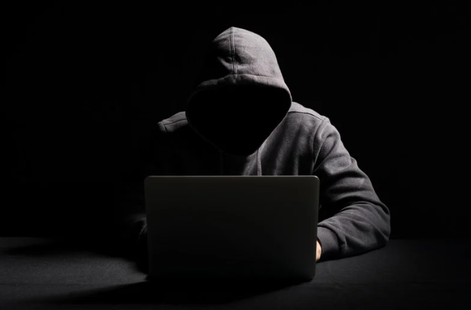 Hooded scammer in front of a laptop