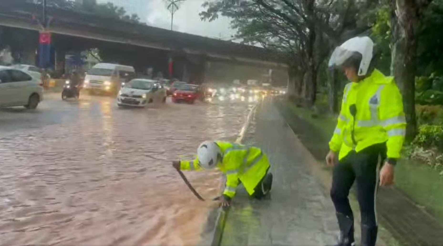 Traffic officers fixing clogged drain in jb with wooden stick