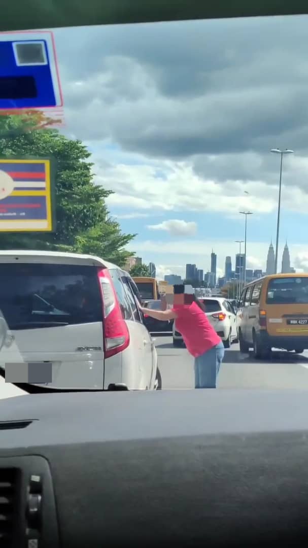 Msian woman aggressively hitting the window of another drivers car.