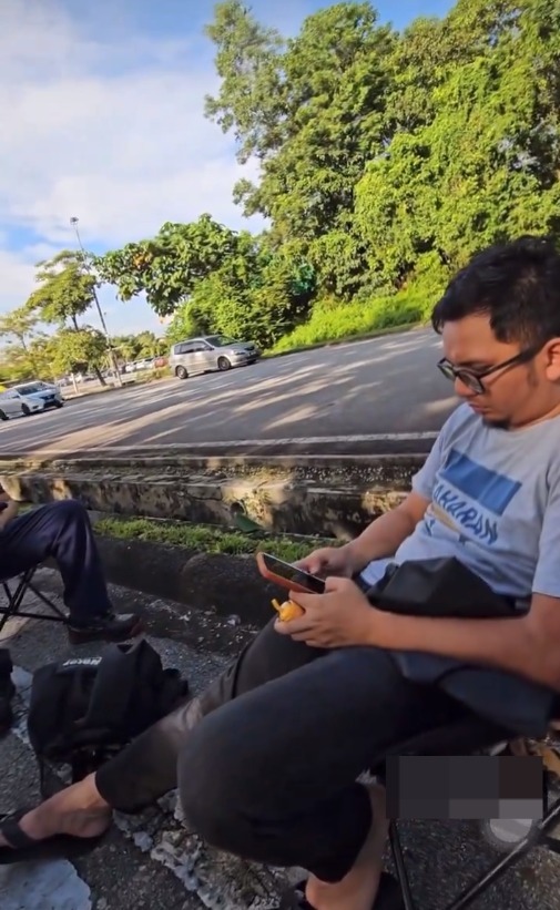 Msian man using his phone sitting by the roadside