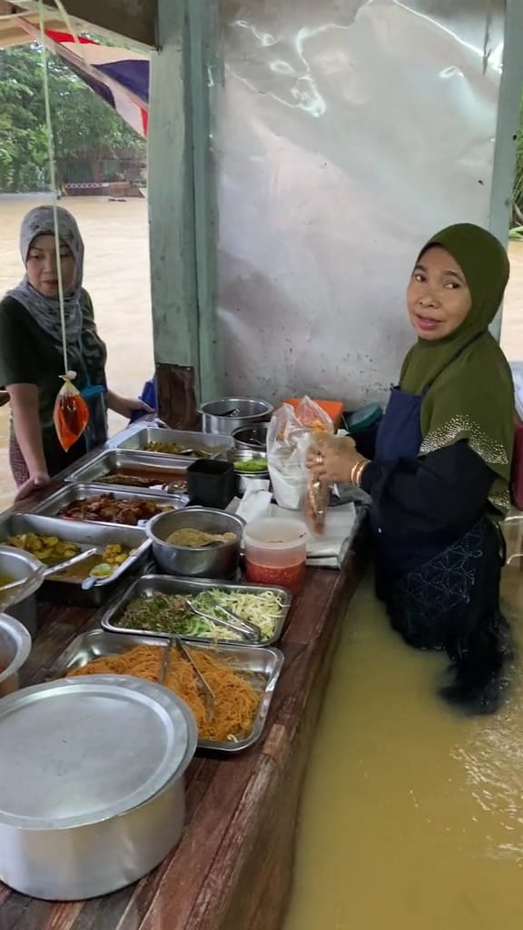 A woman food vendor still chooses to continue doing her food business despite the knee-level flood water.