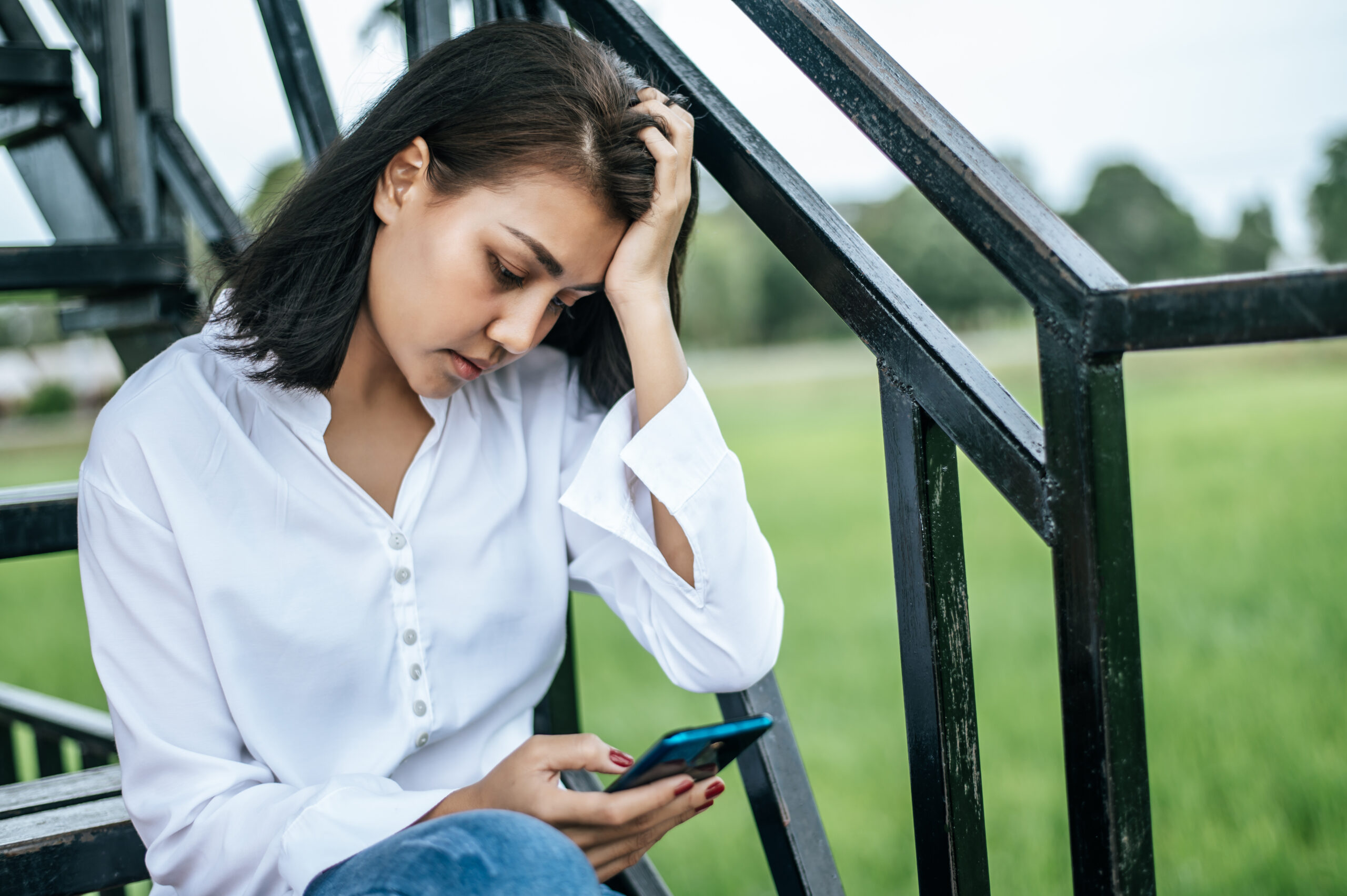 Stressed woman sitting on a ladder looking at a smart phone